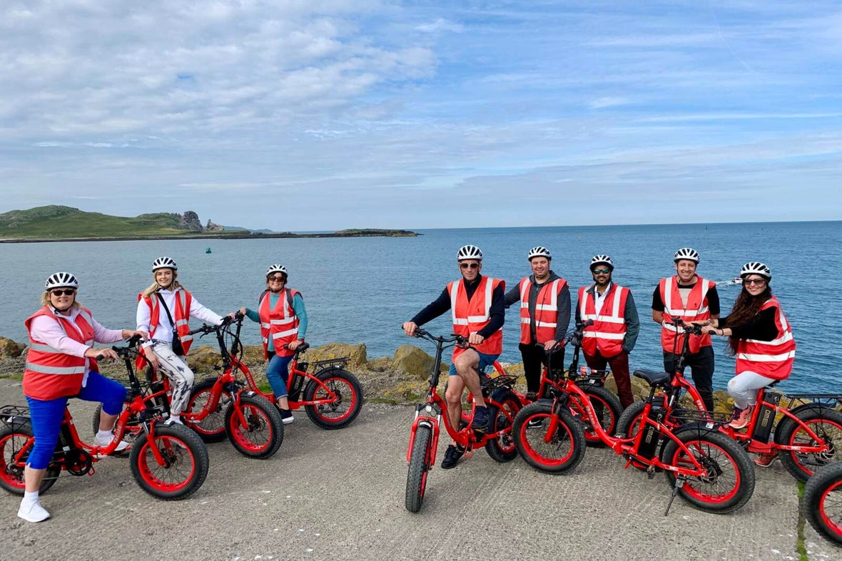 A group of people on a bike tour in Howth, Dublin. Everyone is wearing yellow security vests and helmets with bright orange electric bikes.