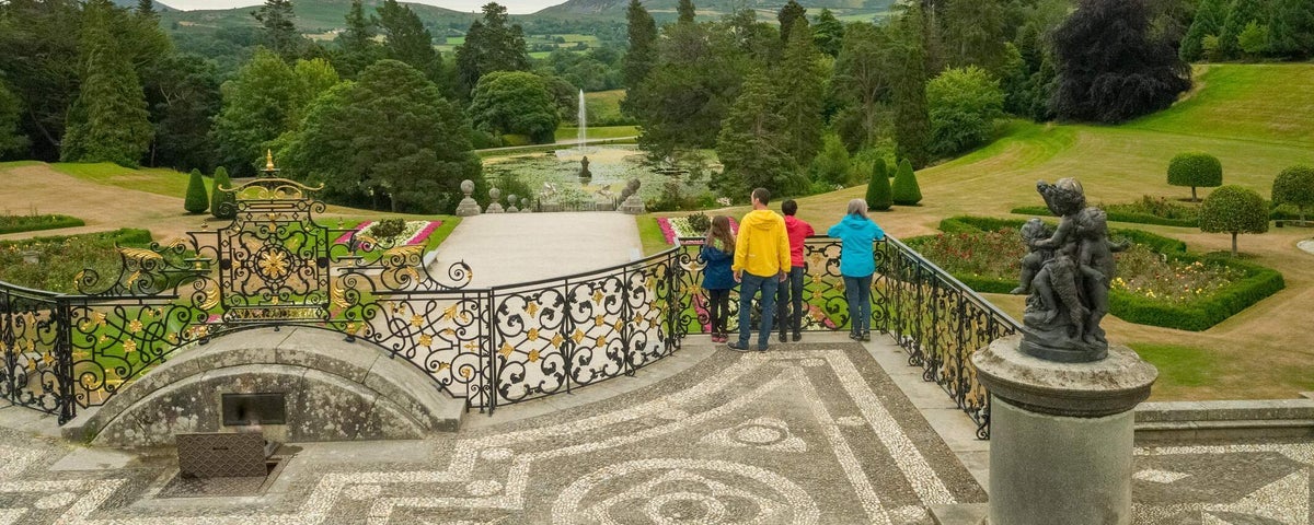 A small tour group standing on a balcony overlooking a decorative garden