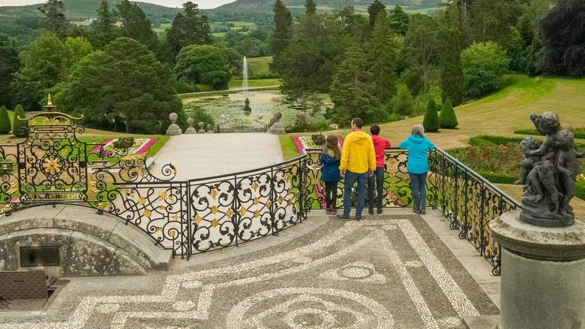 A small tour group standing on a balcony overlooking a decorative garden