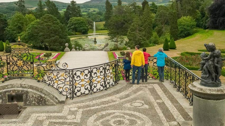 A small tour group standing on a balcony overlooking a decorative garden
