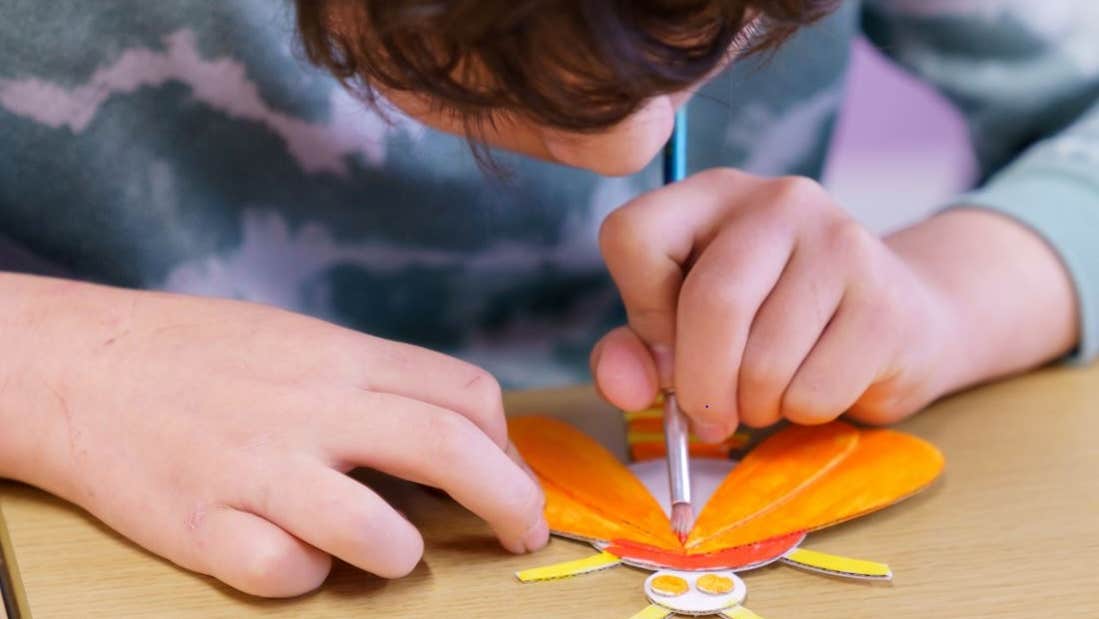 Children's art workshop with Cas McCarthy, a child leaning over a small piece of art work, painting.