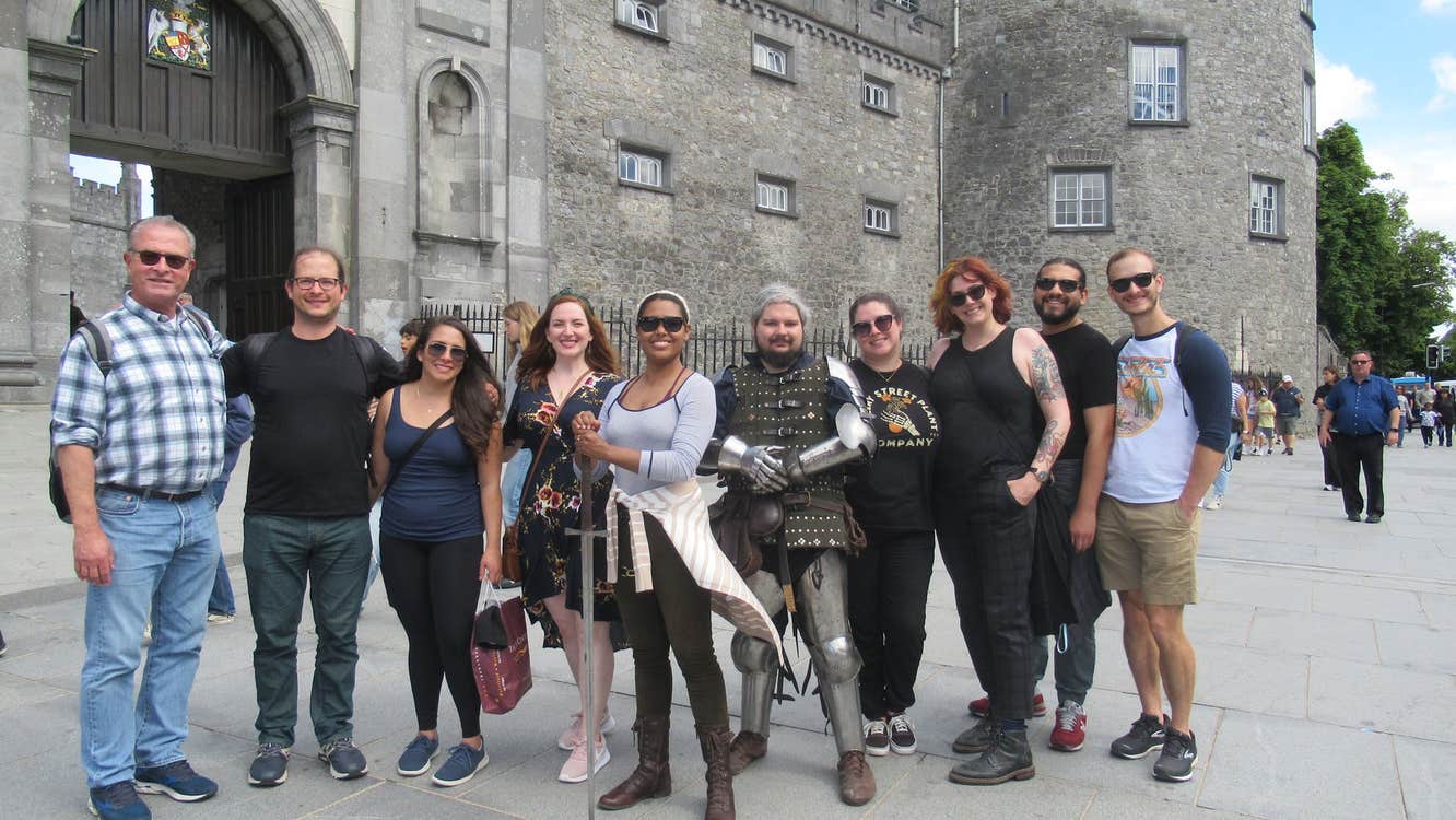 Tour group posing outside a castle with their tour guide dressed as a knight