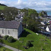 An old church on a small hill overlooking a town with the sea in the distance