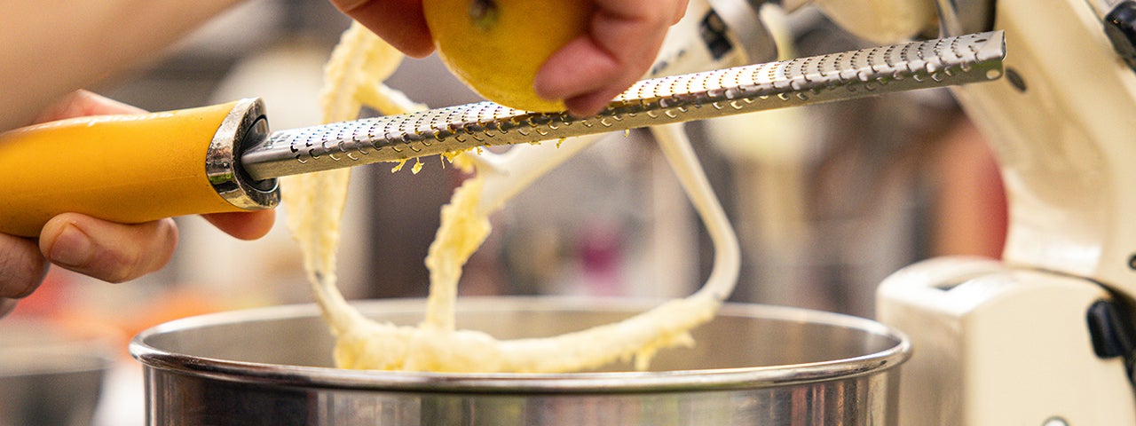 Christmas Cakes & Sweet Treats. A pair of hands grating a lemon into a large mixer bowl.