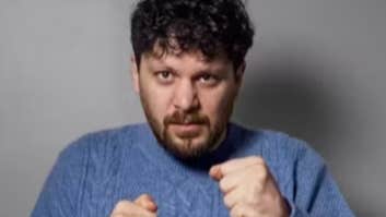 A man in blue knitted jumper holding his hands up in fists.