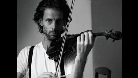 Black and white photo of serious looking man with beard playing a violin.