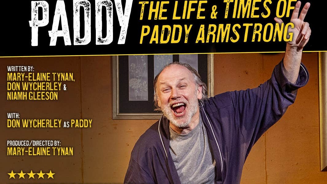 A man in a dressing gown is shouting with arms outstretched on a stage set