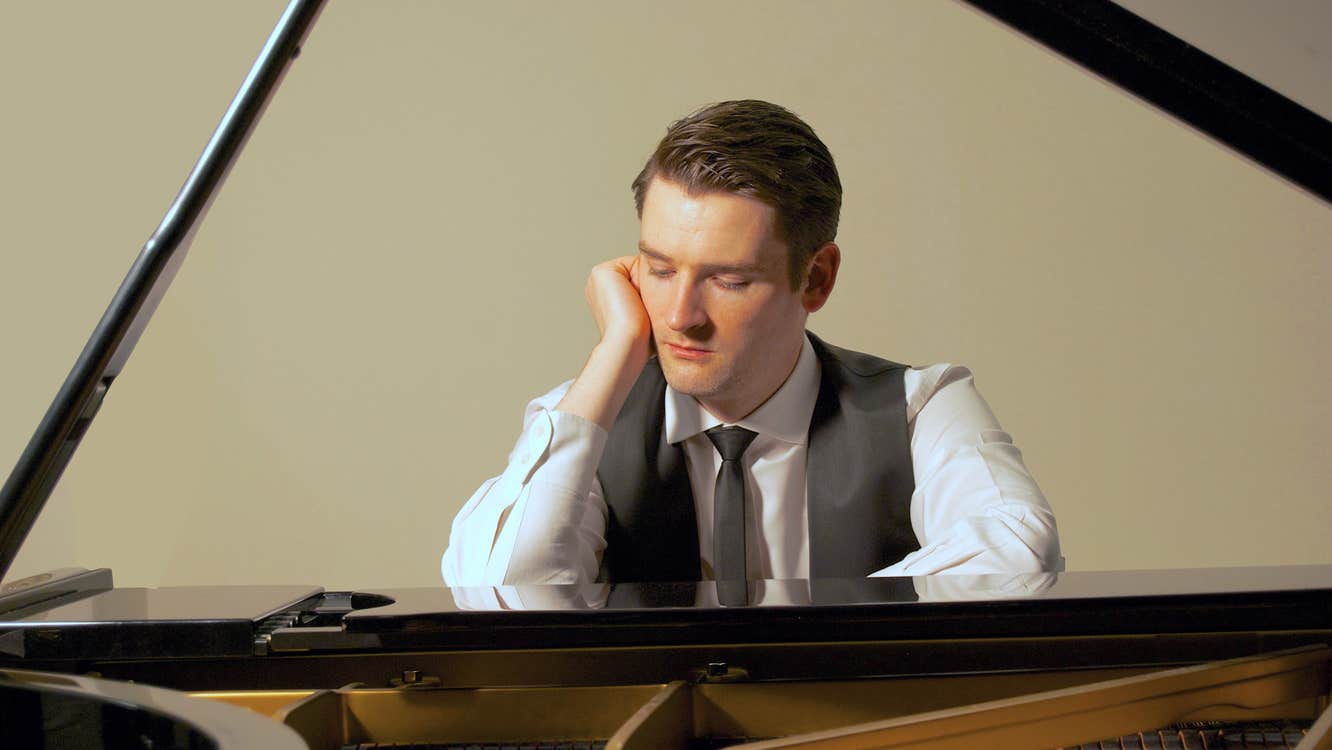Michael McHale is resting his head on one of his hands as he sits pensively at a piano.