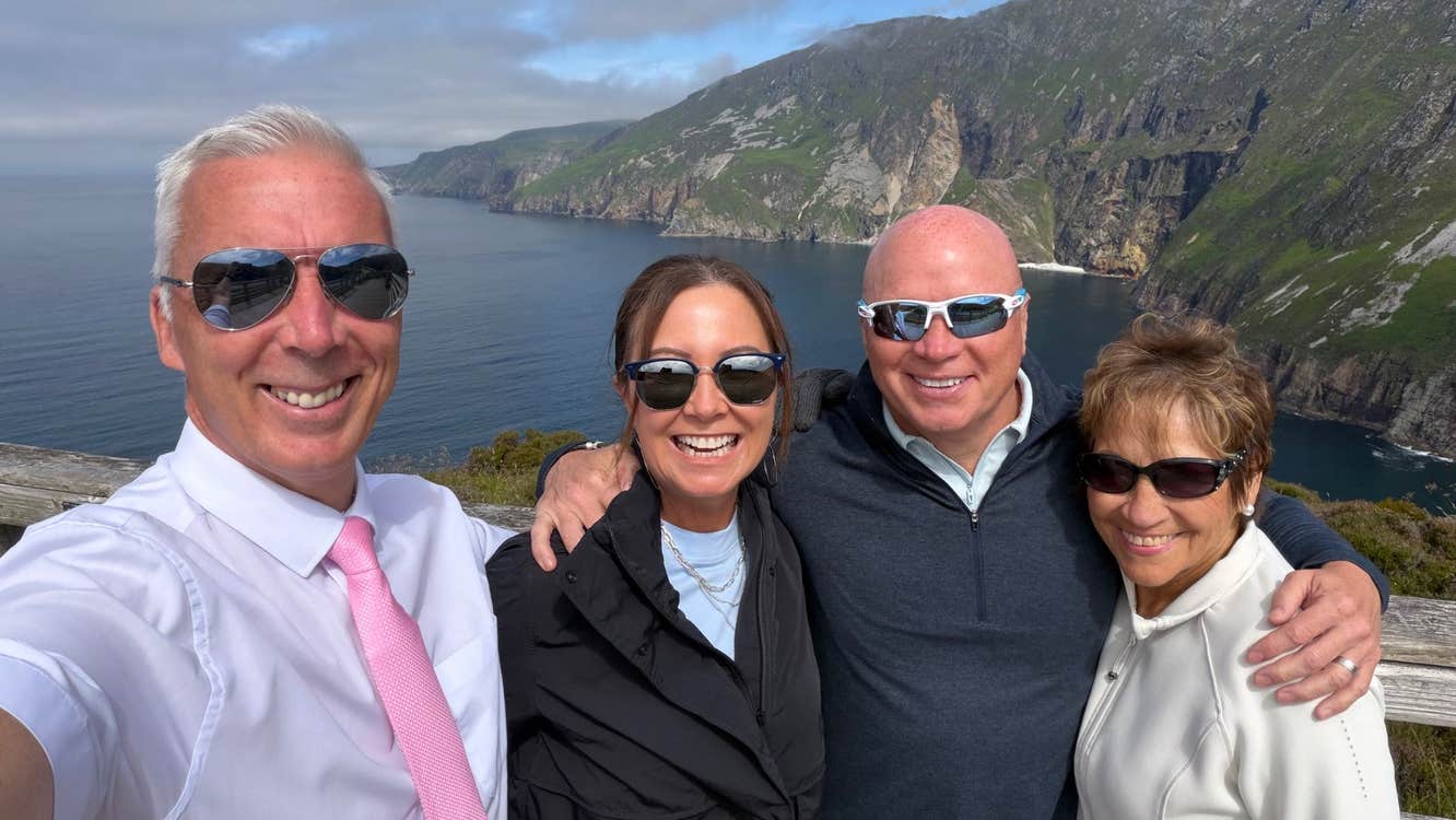 Four people wearing sunglasses pose for a selfie at the Cliffs of Moher