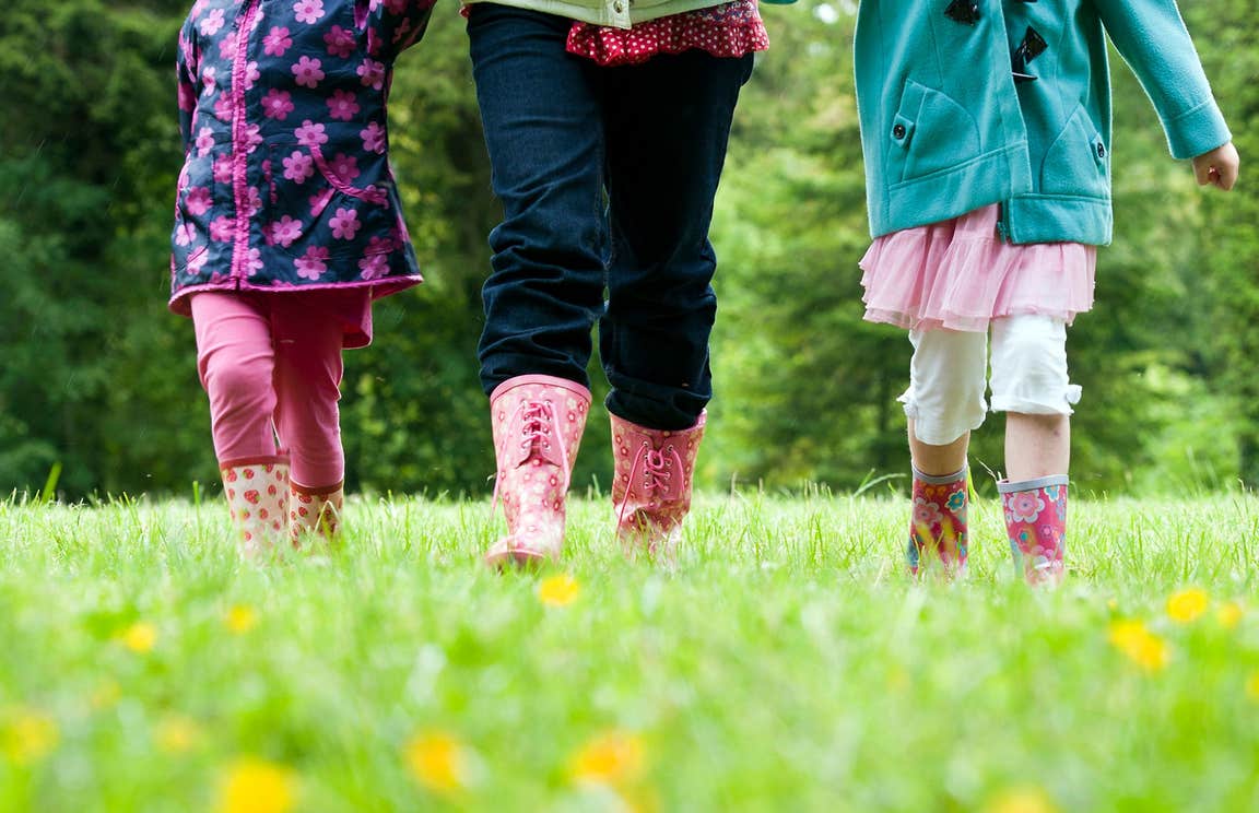 Two children and one adult wearing wellington boots walking in a field of green grass filled with buttercups