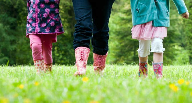 Two children and one adult wearing wellington boots walking in a field of green grass filled with buttercups