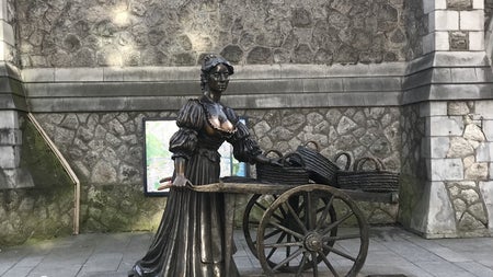 Bronze statue on a street of a lady holding a wheelbarrow