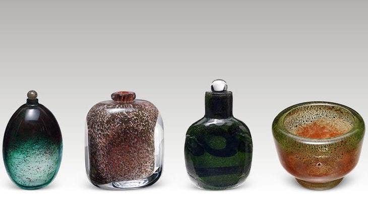 A row of 4 small different coloured glass vases against plain light grey background.