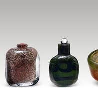 A row of 4 small different coloured glass vases against plain light grey background.