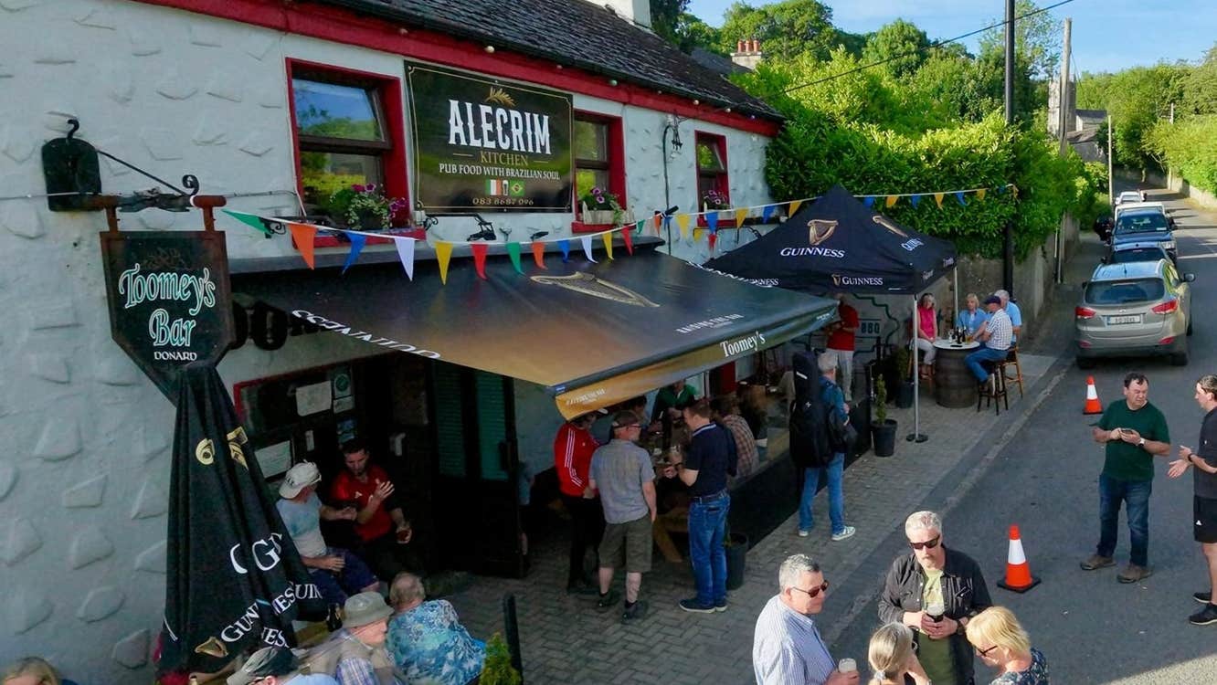 People gathered outside Alecrim Kitchen and Toomey's Bar with outdoor seating and colourful bunting