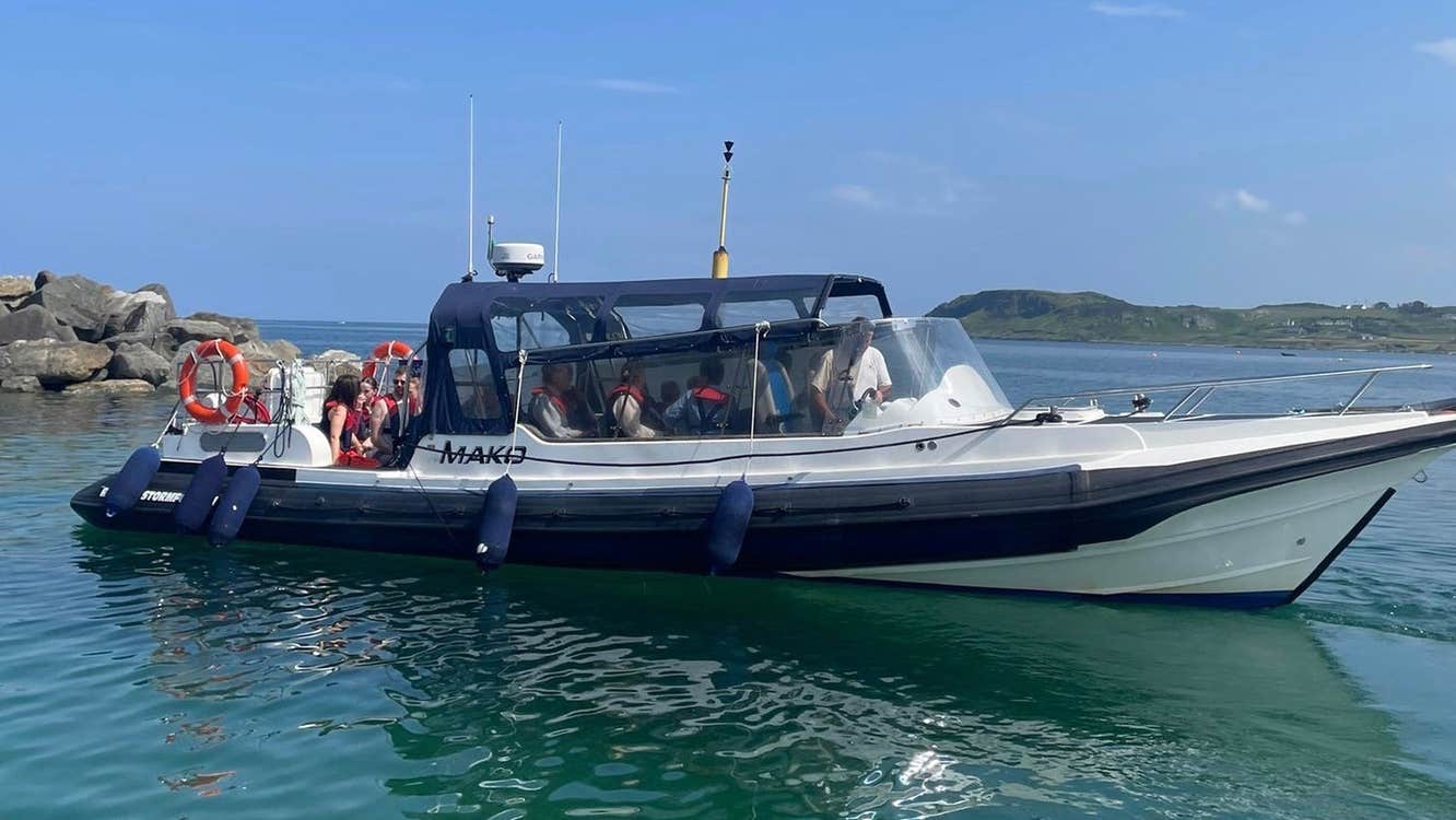 A passenger boat cruising on calm blue water with rocky shoreline and green hills in the background