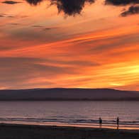 Two people walking on Enniscrone Beach in County Sligo at sunset.