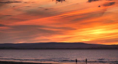 Two people walking on Enniscrone Beach in County Sligo at sunset.