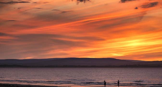 Two people walking on Enniscrone Beach in County Sligo at sunset.