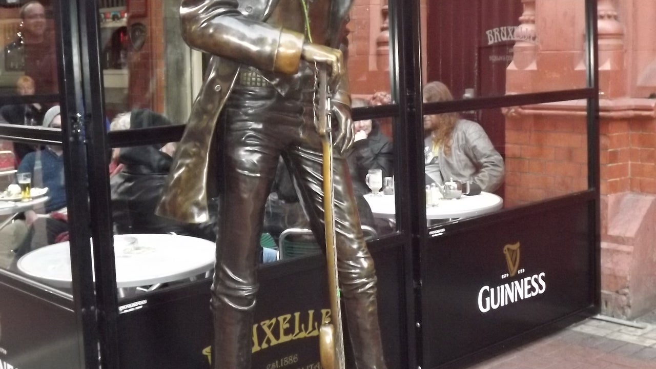 Bronze coloured statue of tall slim man holding a guitar upright in front of him