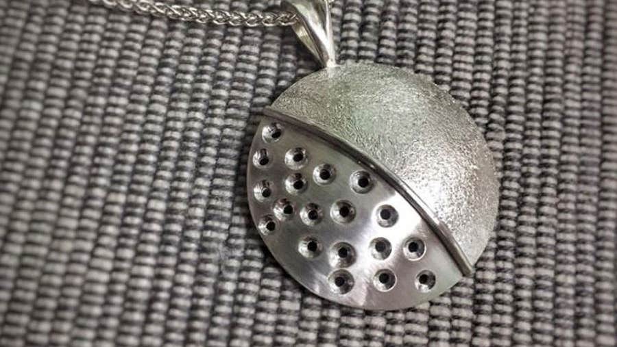 A circular metallic pendant with small holes on one half and a plain design on the other