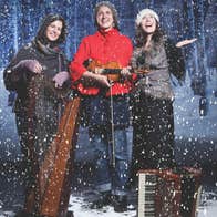3 smiling women standing with musical instruments in snowy scene