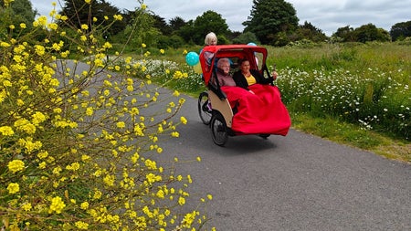 Two people sitting in a trishaw with someone peddling a bike behind them
