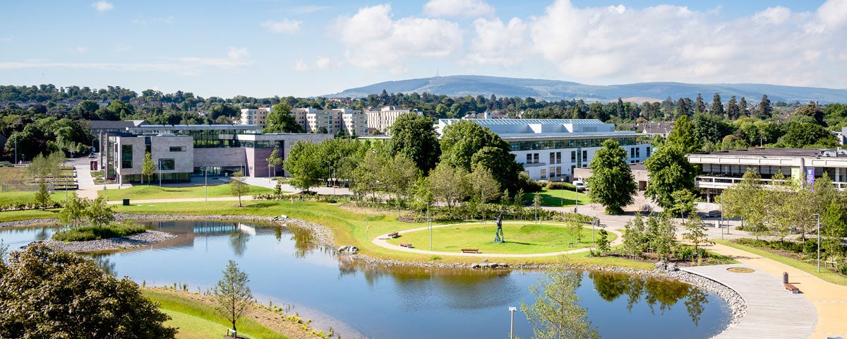 The grounds of University College Dublin with large buildings overlooking a pond and trees