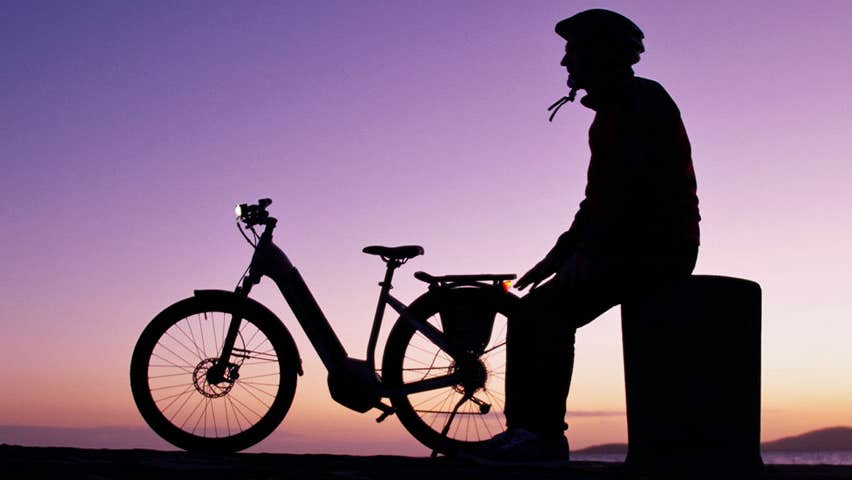 Image of cyclist sitting on pier in the dusk with ebike beside him