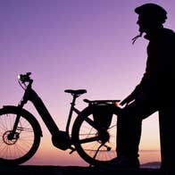 Image of cyclist sitting on pier in the dusk with ebike beside him