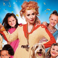 Claire Sweeney as Miss Hannigan in Annie, a woman with rye expression surrounded by 4 young girls and a dog.