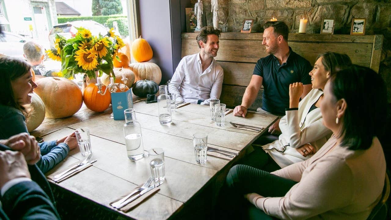 A group of people sitting at a table with pumpkins and sunflowers on the window