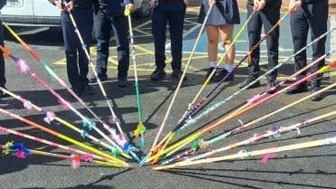 View of lower half of teenagers all holding long, thin, decorated poles into a central point on a playground.