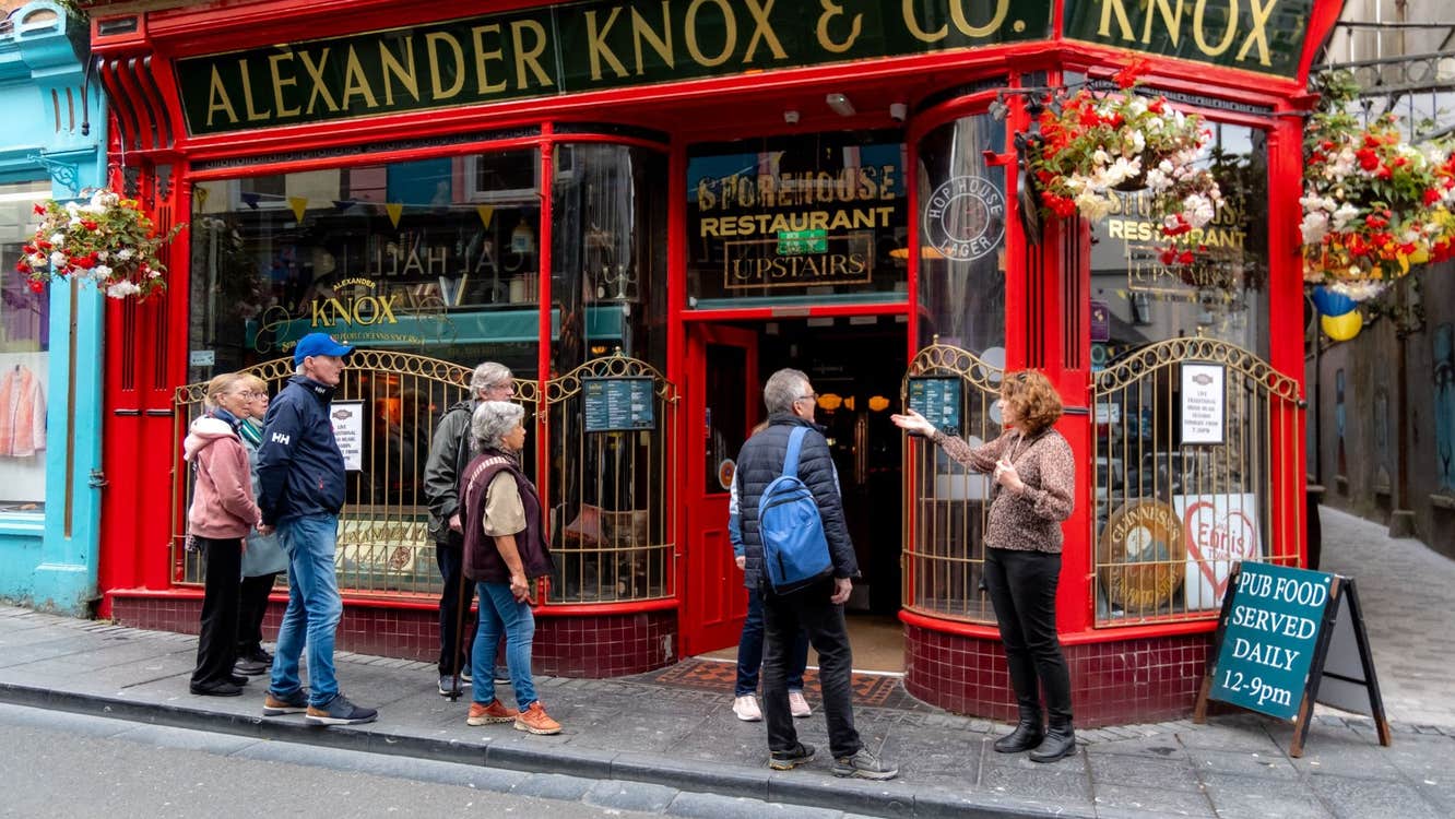 A group of people gather outside a bright red pub on a narrow city street