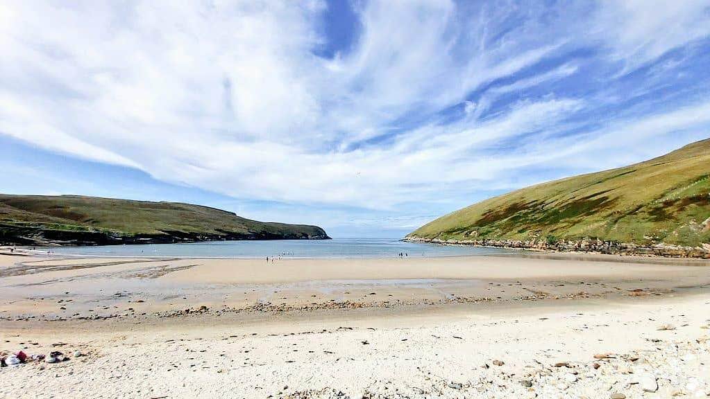 People on a beach and in the water with headlands on either side
