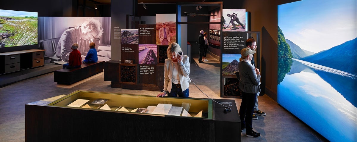 Visitors viewing artefacts in a display case and on AV screens at an exhibition