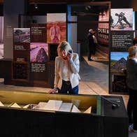 Visitors viewing artefacts in a display case and on AV screens at an exhibition