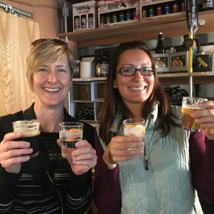 Two people holding a glass in each hand in a beer tasting room
