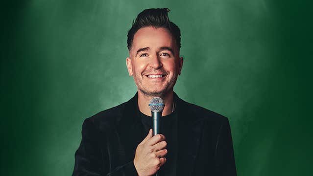 A smiling man holding up a mic to his chin.