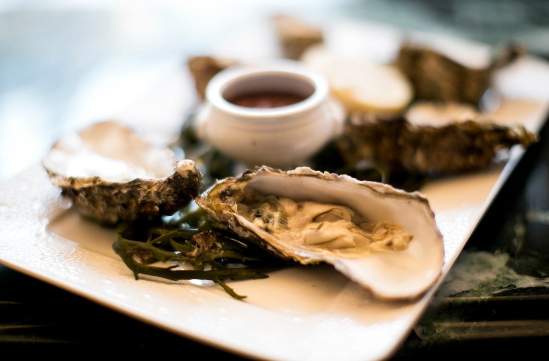 A platter with oysters decorated with seaweed and a small pot of sauce in the middle