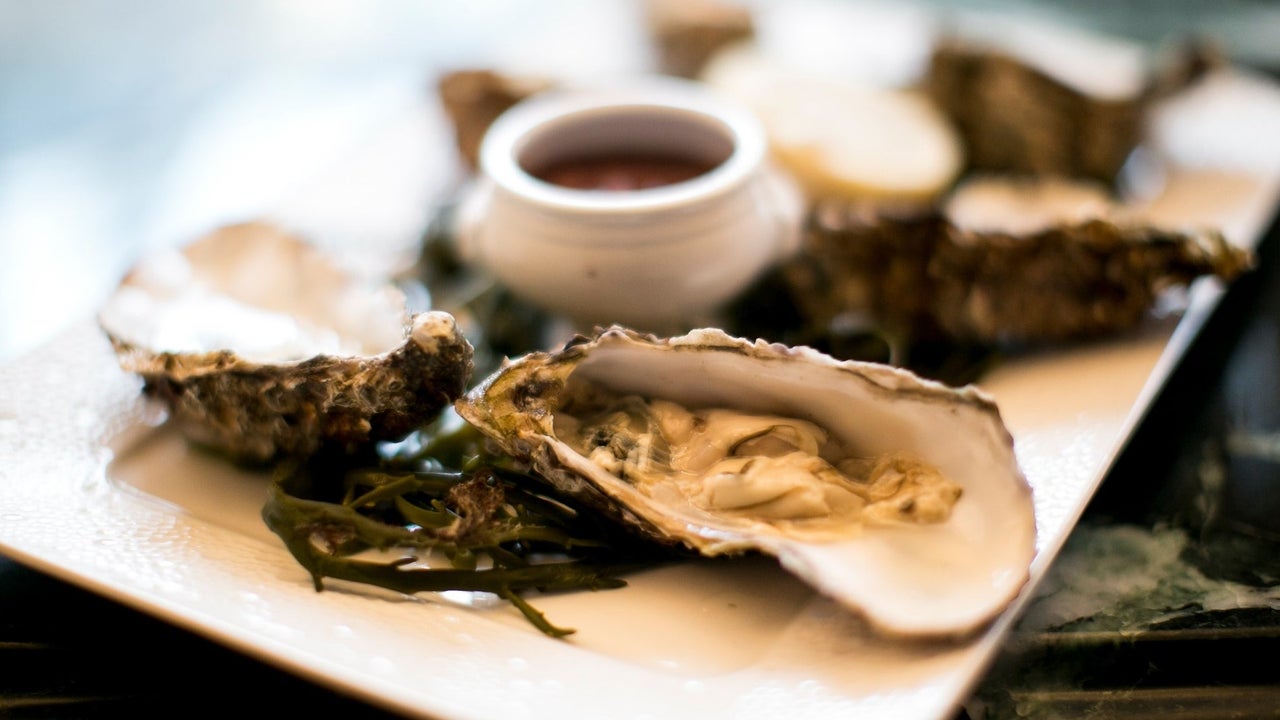 A platter with oysters decorated with seaweed and a small pot of sauce in the middle