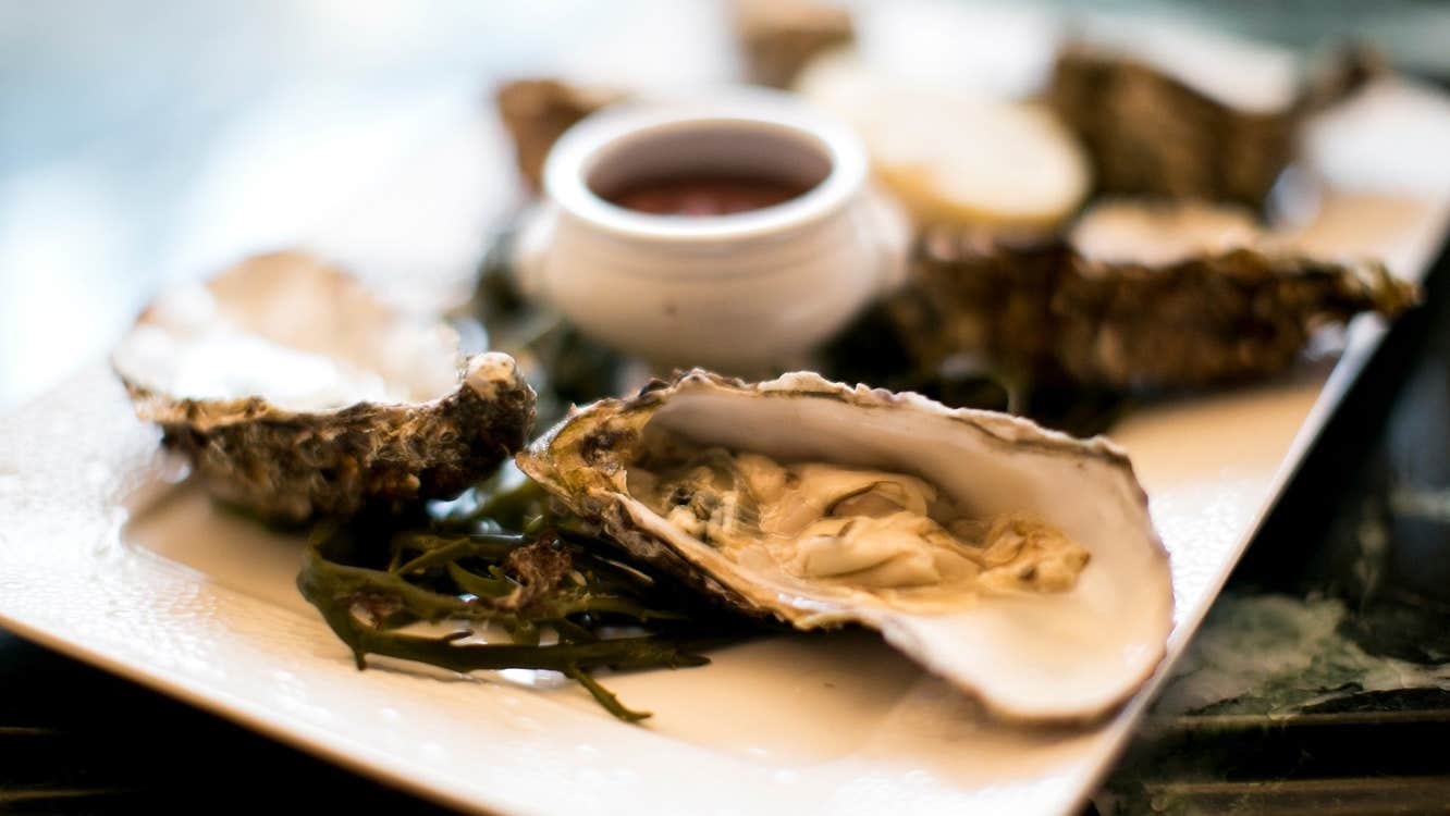 A platter with oysters decorated with seaweed and a small pot of sauce in the middle