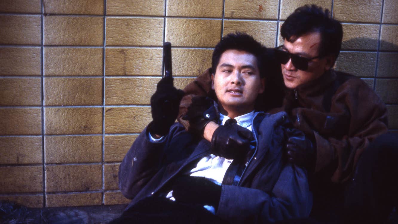 A man with a pistol is on the ground, being held from behind by another man.