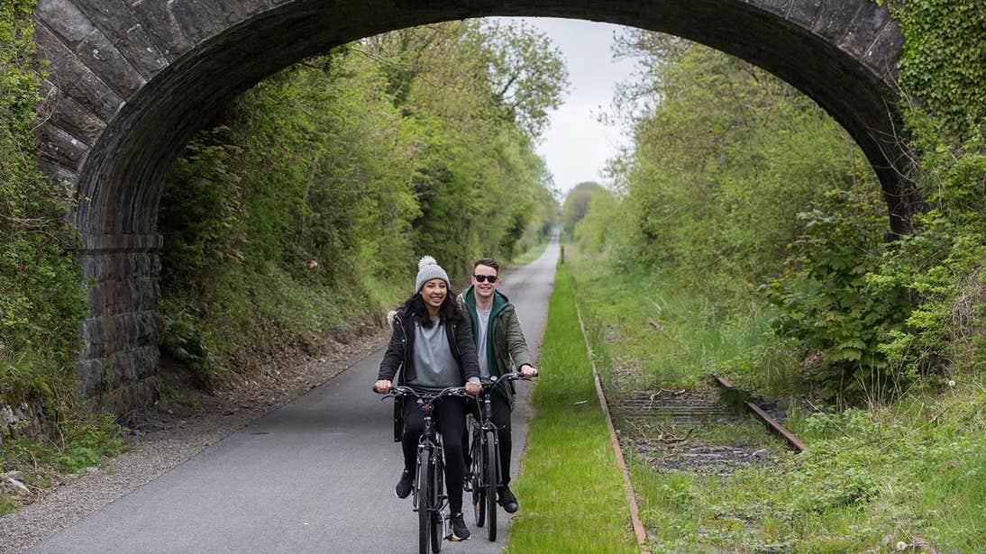 Two people cycling on Old Rail Trail Greenway Athlone Westmeath under a bridge