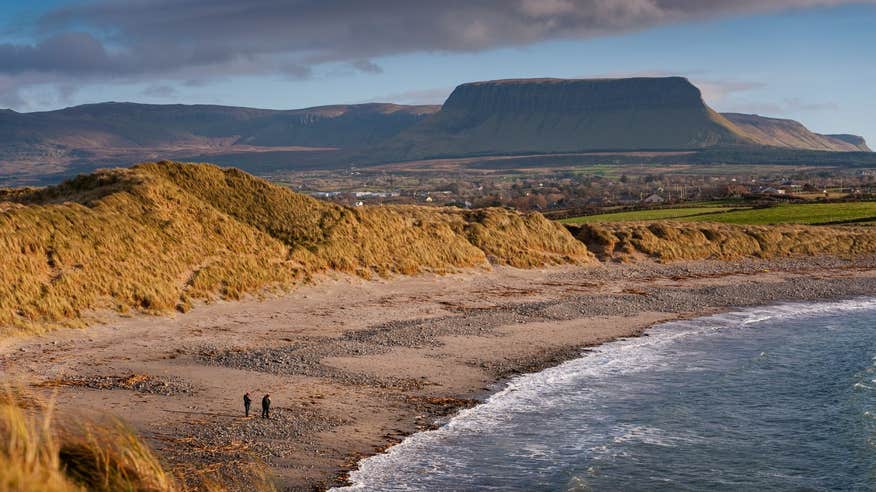 Two people walking Streedagh Beach, Co Sligo with Benbulben in th background.