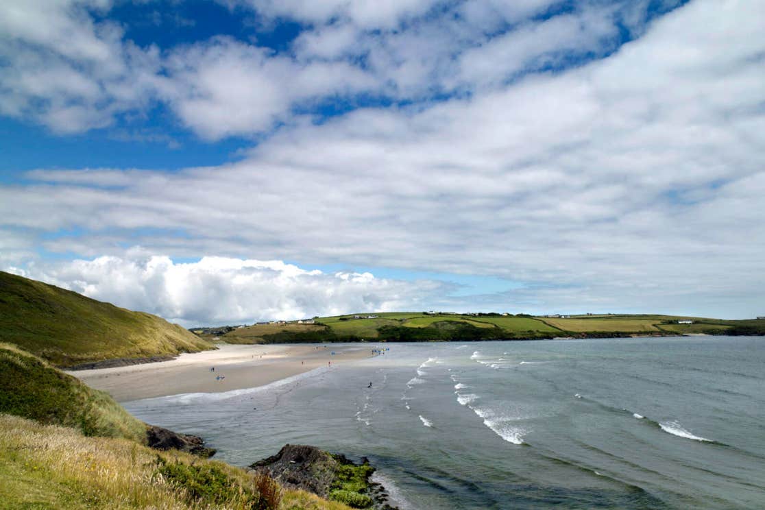 View of Inchydoney Strand with bright green grass, blue sky with some clouds, and the Atlantic ocean lapping at the sand.