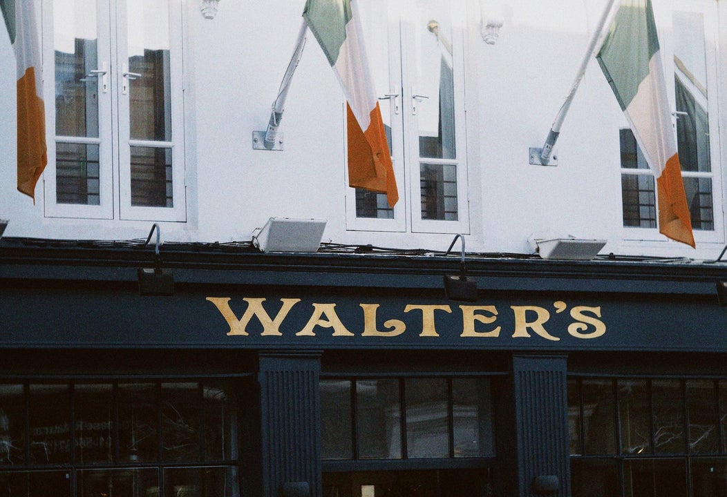 Navy exterior of a pub with gold lettering and three tricolours flying from a white wall