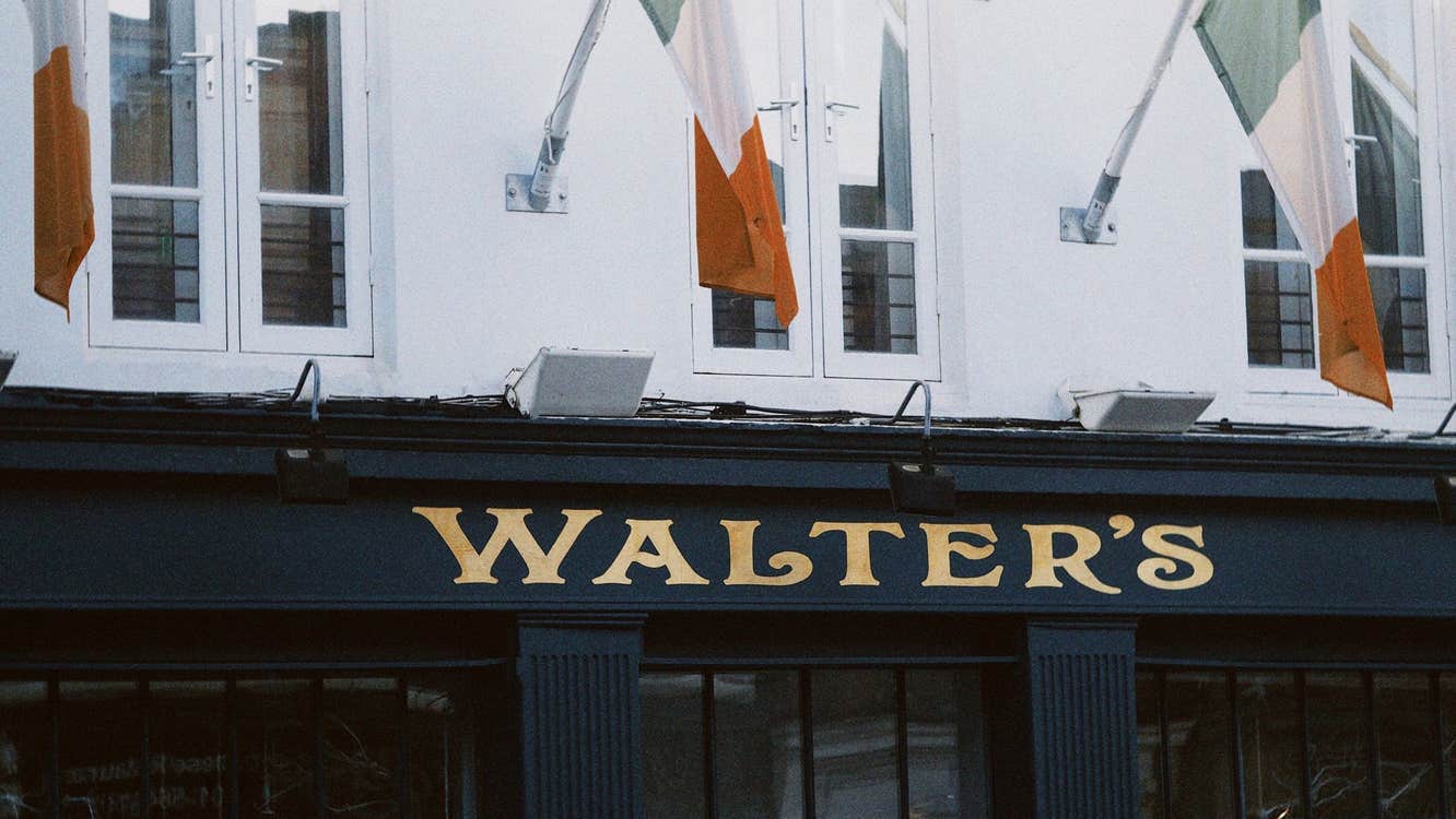 Navy exterior of a pub with gold lettering and three tricolours flying from a white wall