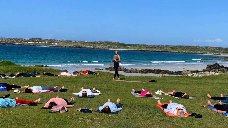 A group of people lying on grass meditating beside a beach with an instructor