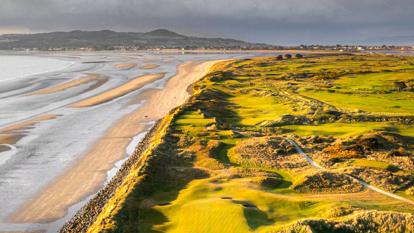 An aerial view of a golf course with sand dunes beside the sea